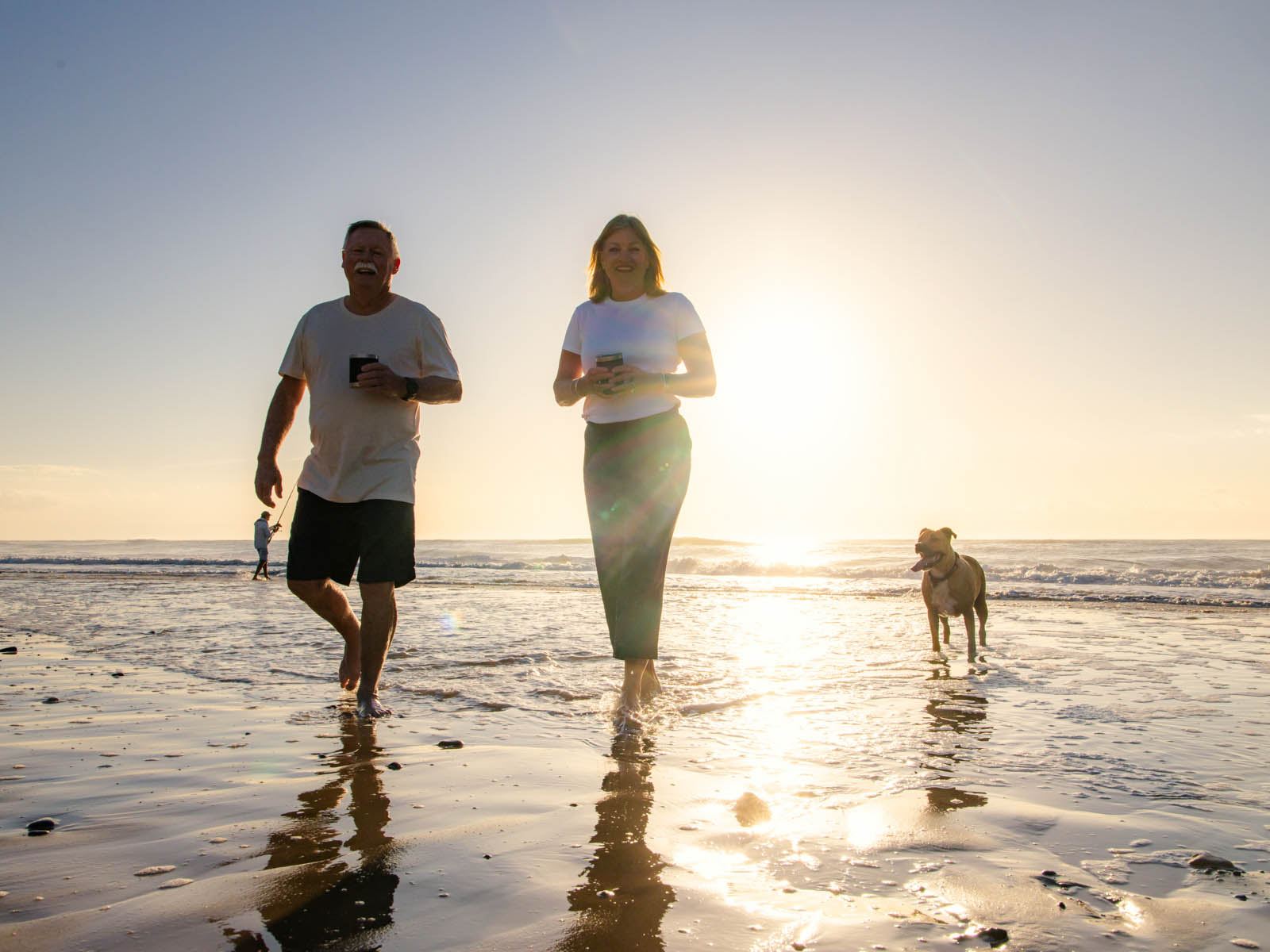 A couple walking a dog on the beach at sunset